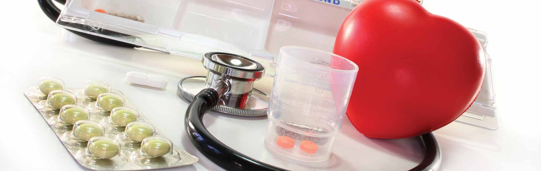 Ein rotes Herz aus Plastik umgeben von Medikamenten und einem Stetoskop.