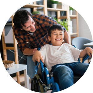 Ein lächelnder Mann schiebt einen fröhlichen Jungen im Rollstuhl.
