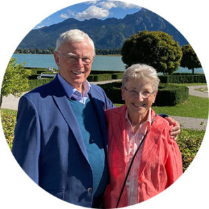 Die beiden Stifter der katharina und Johann Stiftung stehen in einem Park an einem See mit Bergblick.