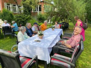 Eine Gruppe Rentner sitzen an Tischen in einem grünen Garten.